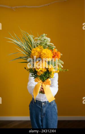 Fille tenant un bouquet de fleurs fraîches debout devant le mur jaune à la maison Banque D'Images