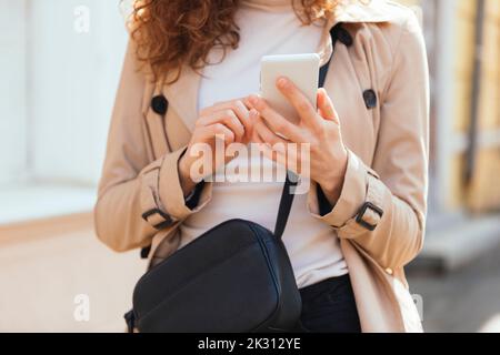 Femme portant un manteau de messagerie texte par smartphone Banque D'Images