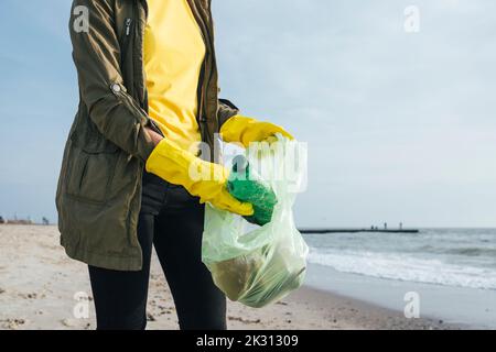 Femme portant des gants collectant les bouteilles de plastique dans un sac à ordures Banque D'Images