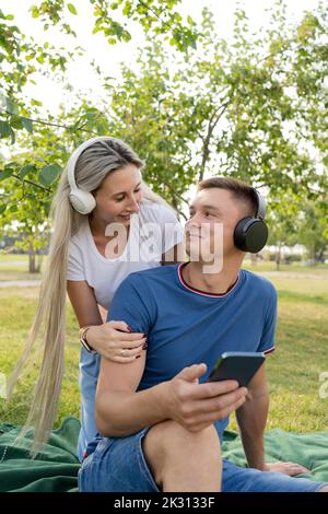 Jeune couple portant un casque pour écouter de la musique dans le parc Banque D'Images
