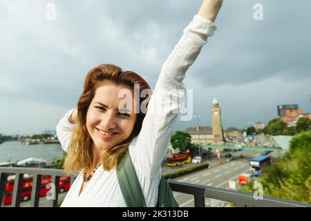 Femme heureuse avec le bras levé debout par la main courante, Hambourg, Allemagne Banque D'Images