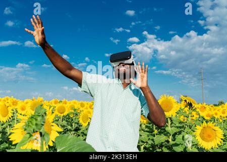 Jeune homme souriant portant un simulateur de réalité virtuelle dansant dans le champ de tournesol Banque D'Images