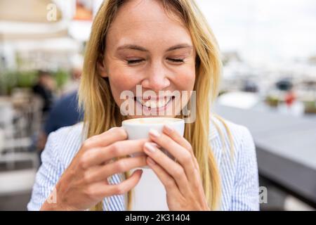 Bonne femme d'affaires avec les yeux fermés tenant une tasse de café Banque D'Images