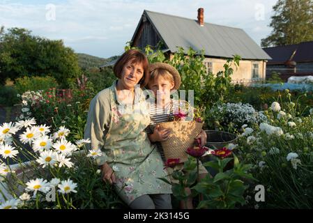 Grand-mère souriante avec petit-fils tenant le panier assis sur la baignoire dans le jardin fleuri Banque D'Images