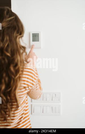 Femme réglant la commande de chauffage au mur Banque D'Images