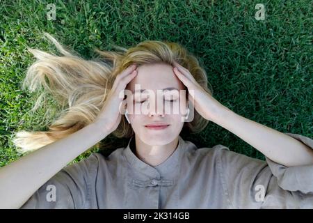 Femme souriante qui écoute de la musique avec des écouteurs intra-auriculaires sans fil posés sur l'herbe Banque D'Images