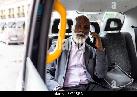 Passager barbu senior parlant sur téléphone portable en taxi Banque D'Images