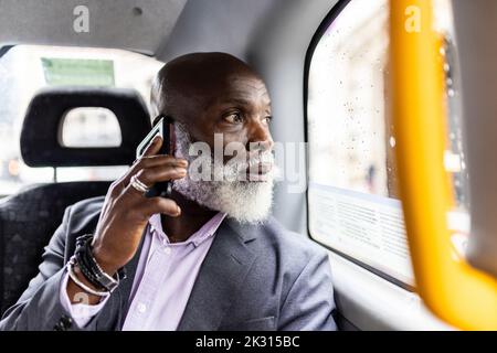 Homme d'affaires senior parlant sur smartphone et regardant par la fenêtre en taxi Banque D'Images