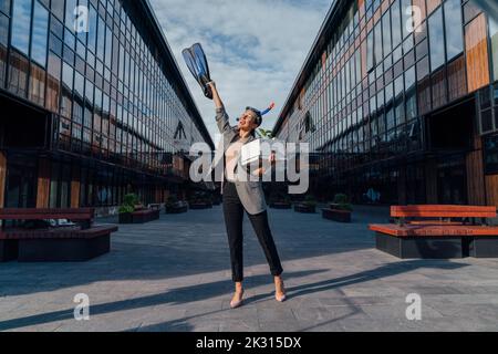 Bonne femme d'affaires avec la main levée tenant le flipper de plongée devant le bâtiment de bureau le jour ensoleillé Banque D'Images