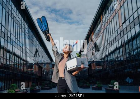 Bonne femme d'affaires avec un flipper de plongée et une boîte devant le bâtiment de bureau Banque D'Images