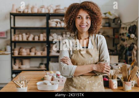 potier souriant portant un tablier debout avec les bras croisés dans l'atelier Banque D'Images
