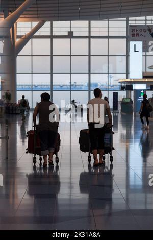 Les voyageurs poussent des chariots de bagages au terminal de l'aéroport international de Haneda, Tokyo, Japon Banque D'Images