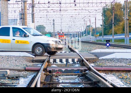 Kemerovo, Russie - 01 septembre 2022. Une voiture de taxi qui se hourra dangereusement traverse un passage de chemin de fer en face d'un train qui s'approche, attention sélective Banque D'Images