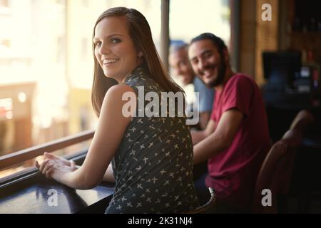 Étaient prêts pour le week-end. Portrait d'une jeune femme souriante dans un bar avec quelques amis. Banque D'Images