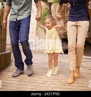 Yippee était en train de vivre une aventure. Une petite fille tenant les mains de ses parents pendant une sortie. Banque D'Images