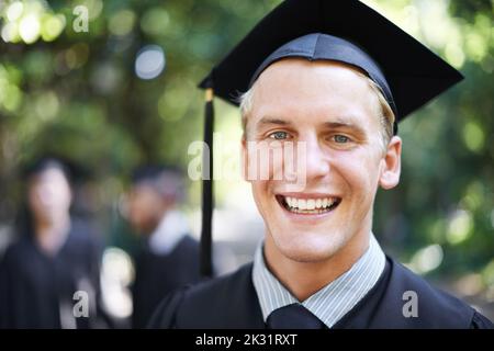 J'ai attendu toute ma vie pour cette journée. Portrait d'un homme heureux étudiant le jour de la remise des diplômes avec d'autres étudiants en arrière-plan. Banque D'Images