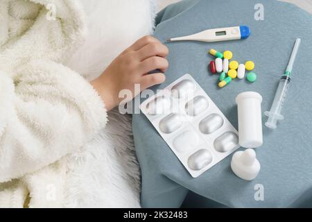 Une fille prend un thermomètre de la table où sont les médicaments. Concept médical. Banque D'Images