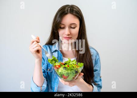 Belle jeune femme mange de la salade avec de la laitue, de la tomate et des olives Banque D'Images