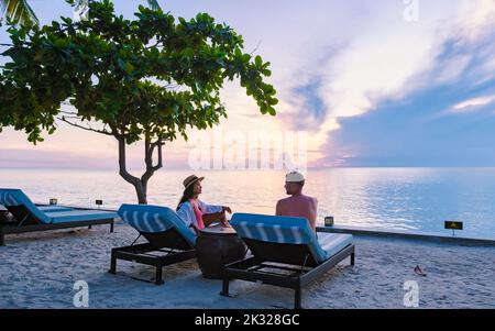 Deux hommes et femmes se détendent au bord de la piscine dans des chaises de plage, une piscine tropicale et une piscine avec des palmiers à la plage donnant sur l'océan Banque D'Images