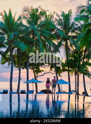 Deux hommes et femmes se détendent au bord de la piscine dans des chaises de plage, une piscine tropicale et une piscine avec des palmiers à la plage donnant sur l'océan Banque D'Images