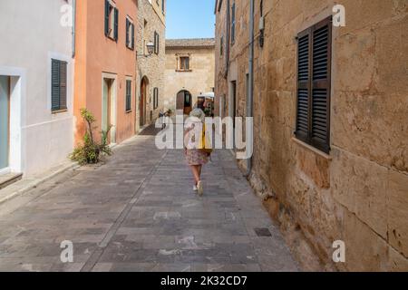 Femme vue de derrière, avec un chapeau, un sac et une robe colorée, marchant le long d'une rue typique dans la ville Majorcan d'Alcudia, le matin ensoleillé d'été Banque D'Images