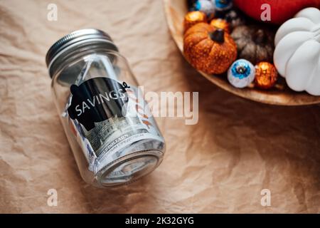 Économisez de l'argent Halloween, économisez, Halloween sur le budget. Pot de maçon en verre avec banque de piggy de dollars sur fond de décoration de citrouille d'Halloween Banque D'Images