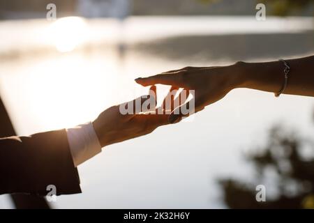 La mariée atteint le marié avec la toile de fond d'un beau lac au coucher du soleil Banque D'Images