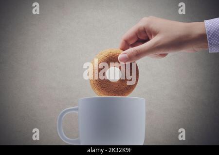 Femme trempant un biscuit en forme de beignet dans une tasse, elle prend le petit déjeuner ou un en-cas, un espace de copie, isolé sur fond gris Banque D'Images
