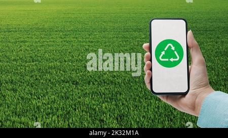 Femme tenant un smartphone avec symbole de recyclage sur l'écran et de l'herbe en arrière-plan, la technologie et le développement durable Banque D'Images