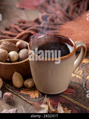 Tasse de café chaude sur un tapis d'automne avec un bol de noix mélangées et une couverture en arrière-plan Banque D'Images