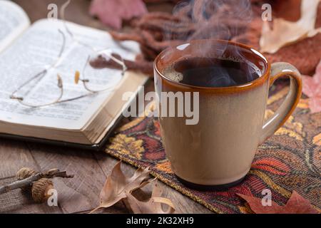 Tasse de café chaude sur tapis d'automne avec livre et couverture en arrière-plan Banque D'Images