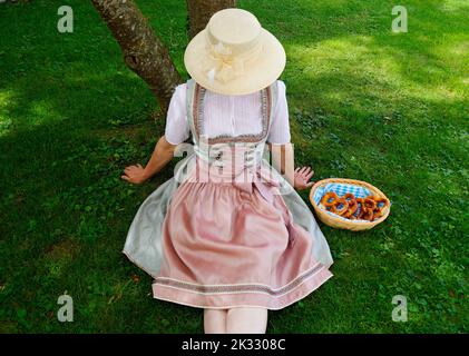 Une femme dans une belle robe traditionnelle bavaroise de dirndl assis sur la prairie verte avec un panier de bretzels ou Brezeln (Munich, Bavière) Banque D'Images