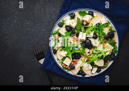 Delicious arugula salad with pears, blueberries, roquefort cheese and walnuts. Black kitchen table background, top view Banque D'Images