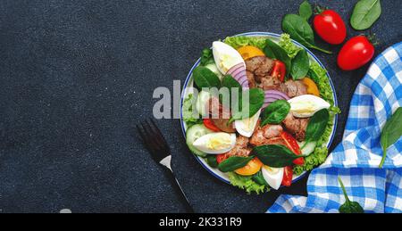 Salade Périgord avec foie de poulet, tomates, concombres, œufs, laitue et épinards. Arrière-plan de la table de cuisine noire, vue du dessus Banque D'Images