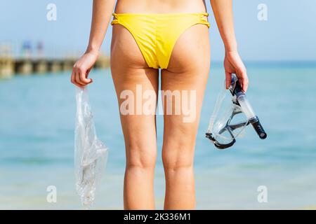 femme en bikini jaune et de la plongée ramasser une poubelle en plastique de la mer Banque D'Images