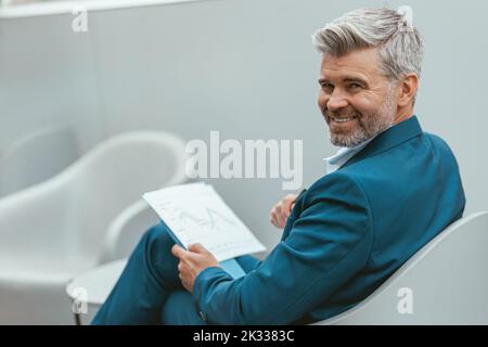 Homme d'affaires souriant et mûr qui travaillait avec des documents tout en étant assis dans un collègue moderne Banque D'Images