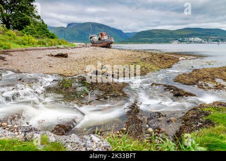 L'eau coule d'un ruisseau vers la rive du Loch Linnhe, près du bateau de pêche toronné, à travers la plage de Caol, avec Ben Nevis comme toile de fond, dans l'Écosse Banque D'Images