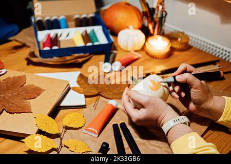 Citrouilles d'automne artisanales. Bricolage artisanat d'automne pour adultes. Les mains des femmes dessinent des motifs sur la citrouille blanche contre le fond de décor d'automne sur la table à la maison Banque D'Images