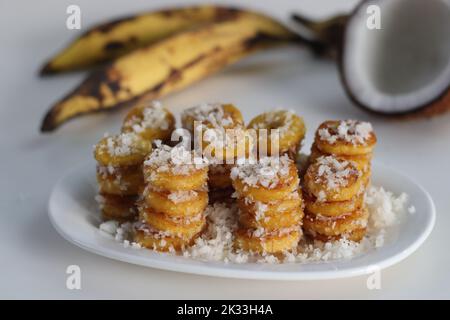 Tranches de plantain mûres rôties au ghee, enrobées de mélange de sucre de coco. Un en-cas spécial du Kerala. Prise de vue sur fond blanc Banque D'Images