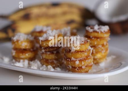 Tranches de plantain mûres rôties au ghee, enrobées de mélange de sucre de coco. Un en-cas spécial du Kerala. Prise de vue sur fond blanc Banque D'Images