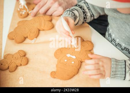 Les mains des enfants peignent un homme de pain d'épice de Noël avec du glaçage Banque D'Images