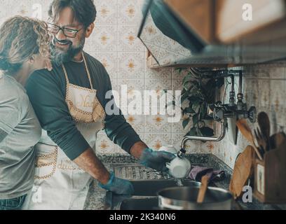 Couple à la maison dans l'activité domestique ensemble laver les plats dans la cuisine. La vraie vie à la maison avec homme et femme matures après le déjeuner. Personnes à l'intérieur Banque D'Images