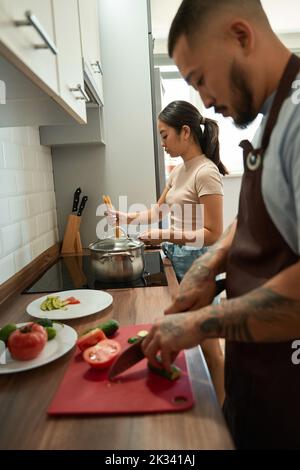 L'homme coupe de la salade, la femme cuit des spaghetti à la maison Banque D'Images