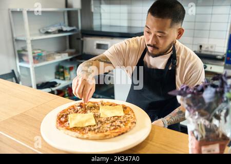 Cuisson ciblée mettant des touches de finition sur la pizza fraîche Banque D'Images