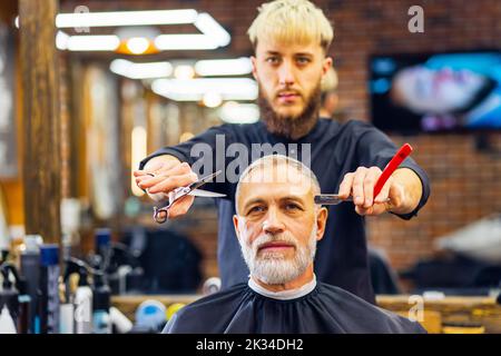 un maître tendance et élégant coupe les cheveux du client de l'homme ancien dans un salon de coiffure moderne Banque D'Images