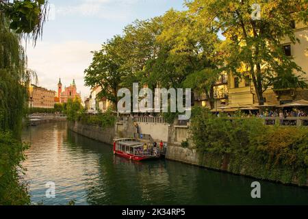 Ljubljana, Slovénie - 3 septembre 2022.Un bateau touristique passe le long de la rivière Ljubljana. Église franciscaine d'Assomption en arrière-plan Banque D'Images