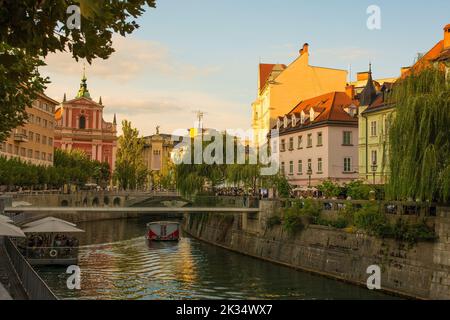 Un bateau touristique passe le long de la rivière Ljubljana, dans le centre de Ljubljana, en Slovénie. Passerelle Fishmarket, Triple Bridge et église franciscaine en arrière-plan Banque D'Images