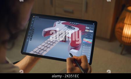 Homme travaillant à la maison à distance et créant 3D prototype de guitare dans un programme professionnel à l'aide d'un ordinateur de tablette numérique et d'un stylet Banque D'Images