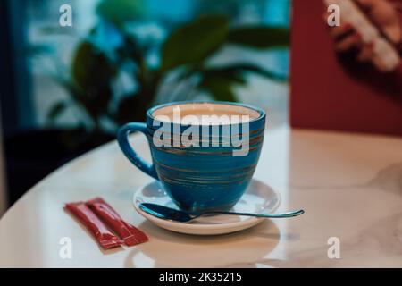 Une tasse de cappuccino sur une soucoupe se tient dans un café sur une table près de la fenêtre Banque D'Images