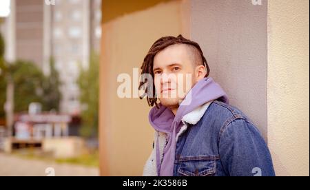 Portrait d'un jeune homme beau avec des dreadlocks posant, debout, appuyé contre un mur dans la rue Banque D'Images
